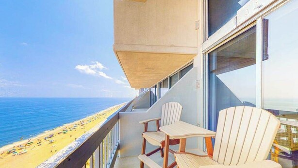 Un balcón con vistas a la playa, sillas de madera y una mesa.