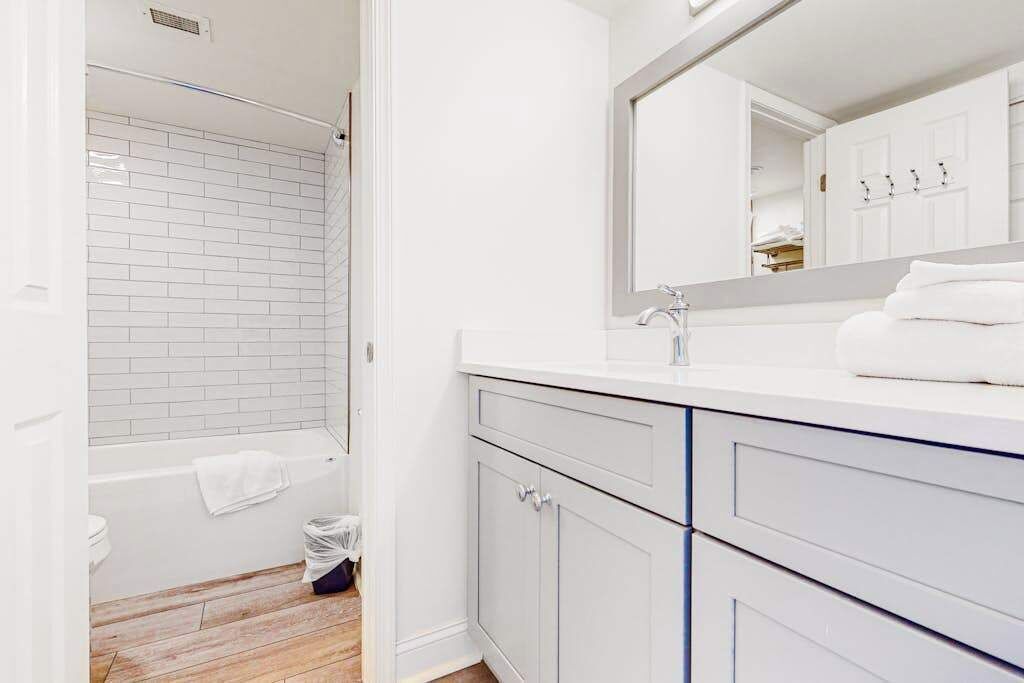A bathroom with white tiles, a bathtub, a sink with a mirror, and a towel on the counter.
