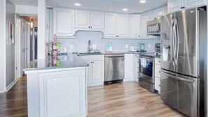 A modern kitchen with white cabinetry, stainless steel appliances, and a central island. - Calypso 705 (Ocean City)