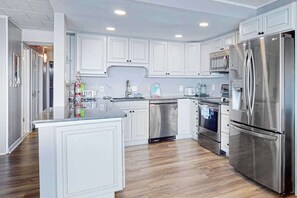 A modern kitchen with white cabinetry, stainless steel appliances, and a central island. - Calypso 705 (Ocean City)
