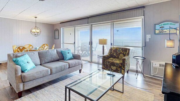 A living room with a sofa, armchair, glass coffee table, ceiling fan, and large windows with a view. - Calypso 705 (Ocean City)