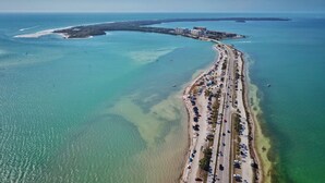 Luftaufnahme einer Küstenstraße mit Strand und Gebäuden in der Ferne.