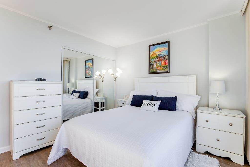 Une chambre à coucher avec un grand lit, une commode, une table de chevet, un miroir et un tableau accroché au mur.