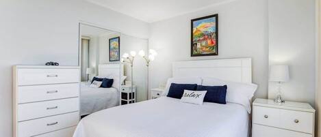 Une chambre à coucher avec un grand lit, une commode, une table de chevet, un miroir et un tableau accroché au mur.