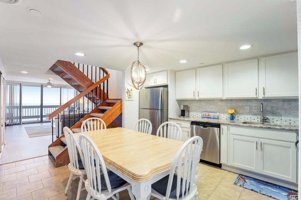 Een moderne keuken met witte kasten, een roestvrijstalen koelkast en een eethoek met een houten tafel en witte stoelen.