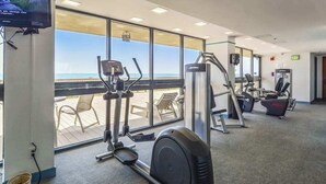 Une salle de sport équipée de machines de cardio, d’un téléviseur et offrant une vue sur la plage.