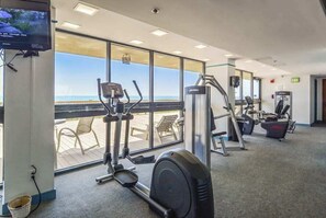 Ein Fitnessraum mit Cardiogeräten, einem Fernseher und Blick auf den Strand.