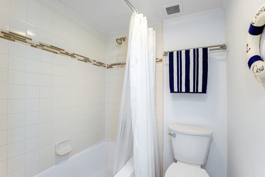 Et badeværelse med badekar, toilet og et håndklædestativ med et stribet håndklæde.