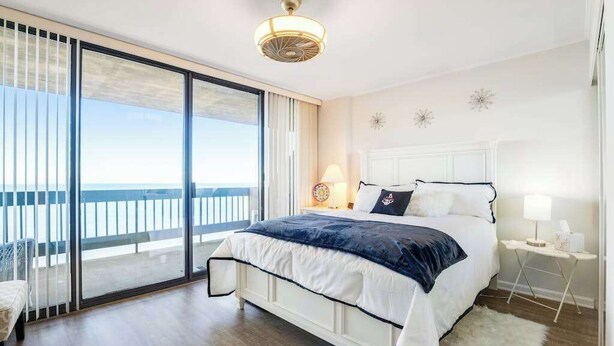 Une chambre avec un grand lit, une table de chevet, une lampe et une vue sur l’océan grâce à de grandes portes coulissantes.