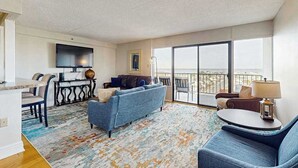 A modern living room with a sofa, chairs, a dining table, and a large window.