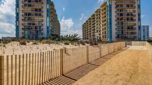 A beachfront hotel with multiple balconies, a sandy walkway, and a wooden fence. - Braemar Towers 1006 (Ocean City)