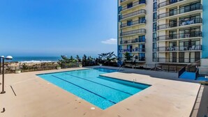 A swimming pool with a view of the ocean, surrounded by a high-rise building with balconies. - Braemar Towers 1006 (Ocean City)