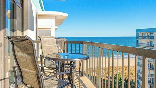 A balcony with a glass table and chairs, overlooking a beach and ocean. - Braemar Towers 1006 (Ocean City)
