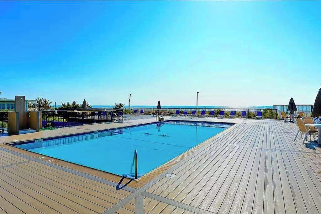 A wooden deck with a swimming pool, lounge chairs, and a view of the ocean.