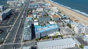 Luftaufnahme einer Küstenstadt mit langem Strand, mehrstöckigen Gebäuden und einer Straße, die parallel zum Strand verläuft.