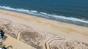 Ein Strand mit sandigem Ufer, einer Holzlattenumzäunung und freiem Blick auf den Ozean.