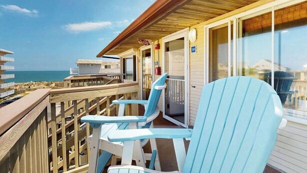 Ein Balkon mit Blick auf den Strand, ein überdachter Bereich mit einem Schild und ein blauer Stuhl.