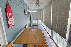Eine überdachte Veranda mit einem Holztisch, einem roten Schild an der Wand und einem Deckenventilator.