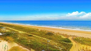 Una playa con cielo despejado, orilla arenosa y una zona cercada con vegetación.
