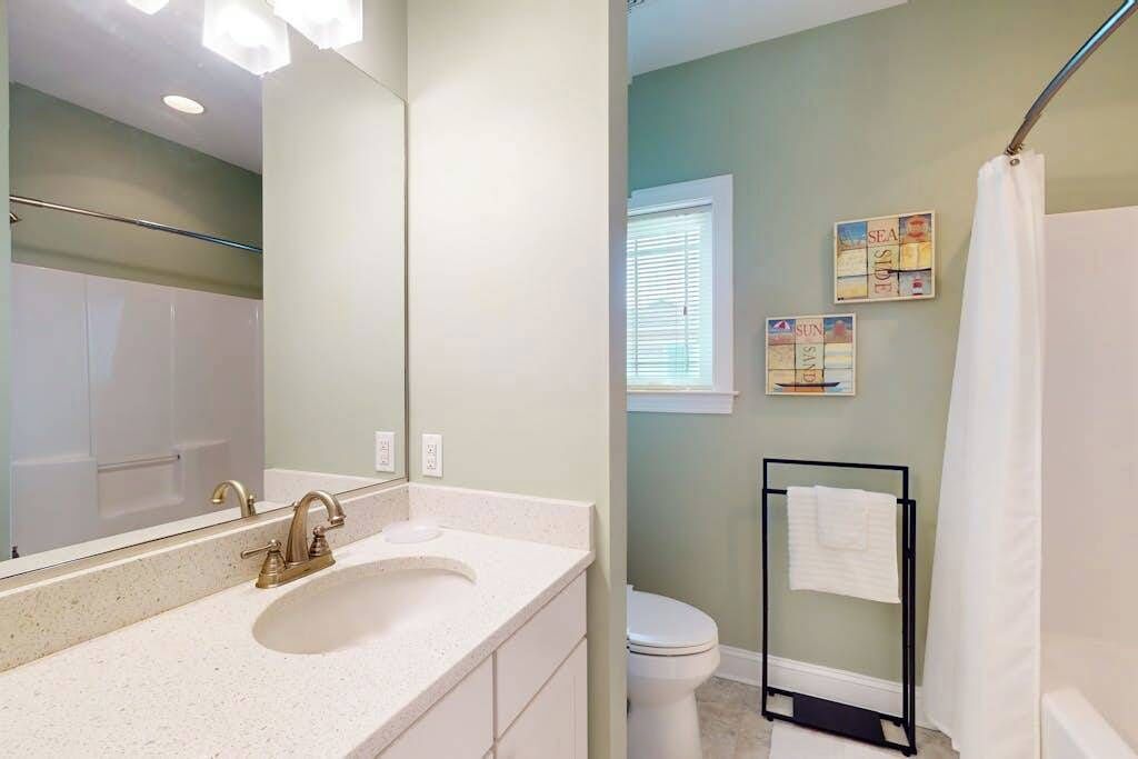 A bathroom with a sink, mirror, toilet, and shower curtain.