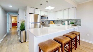Une cuisine moderne avec des meubles blancs, des appareils en acier inoxydable, un grand îlot central doté de tabourets et un pare-feu en carreaux.