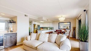 Un salon moderne avec un canapé beige, un coin repas doté d’une table en bois et une cuisine en arrière-plan.