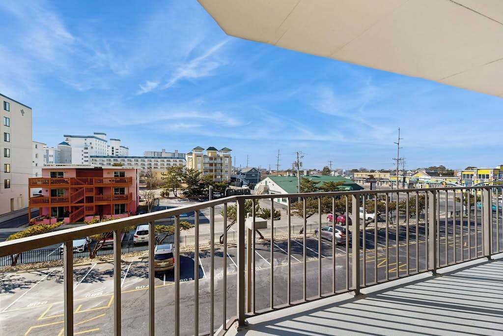 Un balcon donnant sur un parking et sur des bâtiments situés au loin.