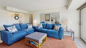 A living room with two blue sofas, a grey ottoman, and a pink carpet. - Third-floor condo in oceanfront building with balcony, pool & beach access (Ocean City)