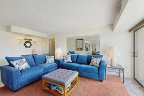 Un salon avec deux canapés bleus, un pouf gris et un tapis rose.