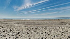 A wide beach with footprints, a clear sky, and distant ocean waves. - Third-floor condo in oceanfront building with balcony, pool & beach access (Ocean City)