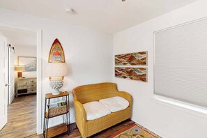 Una habitación con un sofá de mimbre, una lámpara y obras de arte en las paredes.