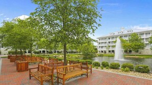 A courtyard with wooden benches, a fountain, and a building with multiple balconies. - Sunset Island - 35 Fountain 4D (Ocean City)