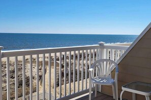 A balcony with a white chair and table, overlooking a beach with a wooden fence. - Ocean-view townhome with easy beach access & large deck (Ocean City)
