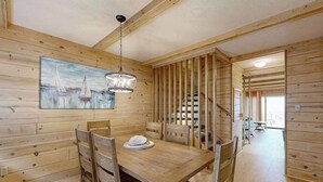 Een houten interieur met een eettafel, stoelen, een schilderij en een trap.