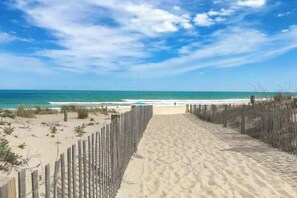 Ein sandiger Strandweg führt zum Meer, begleitet von einem Holzzaun.