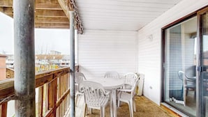 Un espacio al aire libre cubierto con una mesa, sillas, baranda de madera y puerta de cristal que da a un balcón.