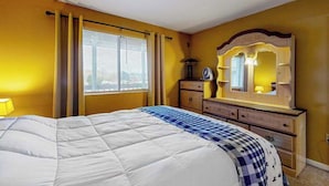 Una habitación de hotel con cama, cómoda, espejo y ventana con cortinas.