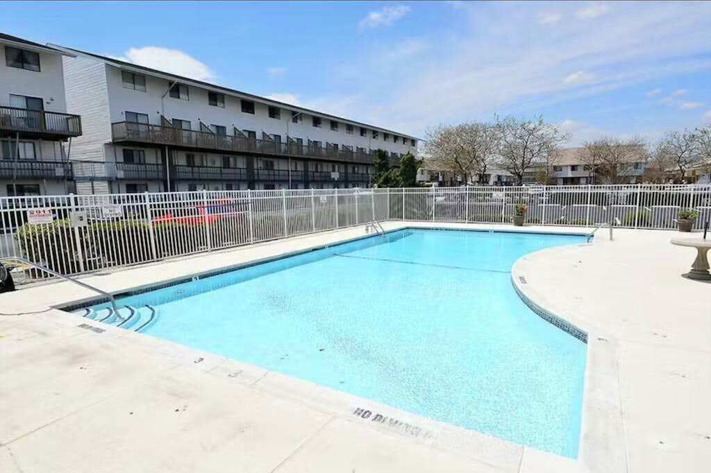 A rectangular swimming pool with a white fence, surrounded by a building with balconies.