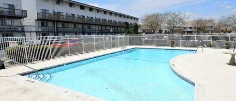 A rectangular swimming pool with a white fence, surrounded by a building with balconies.