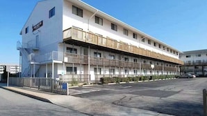 Un motel con una estructura de dos pisos, un estacionamiento cercado y cielo despejado.