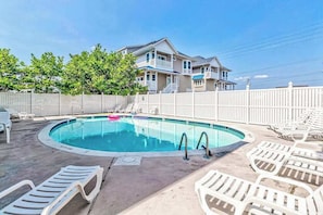 A swimming pool with lounge chairs, a white fence, and a two-story house in the background. - Peek-a-Boo Oceanview Condo with Shared Pool & Prime Location 1 Block from Beach (Ocean City)