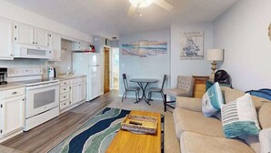 Een compacte leefruimte met kitchenette, eethoek en een bank met kussens.