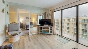 Un soggiorno moderno con televisione, un divano e un'ampia finestra vista su un edificio.