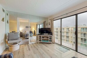 A modern living room with a television, a sofa, and a large window with a view of a building. - Wight Bay North 544 (Ocean City)