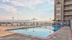 Una piscina con vista sull'oceano, una terrazza recintata e un edificio con il logo di una barca a vela.