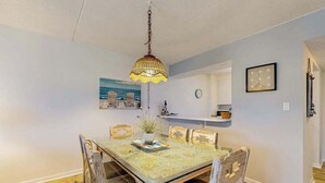 Un'area pranzo con un tavolo in vetro, sedie in legno, una lampada a sospensione, un quadro appeso e una sveglia.
