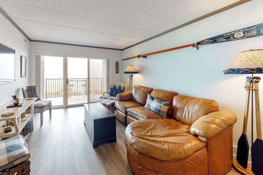 Ein Wohnzimmer mit Ledersofa, einem kleinen Tisch, einer Lampe und Blick ins Freie.