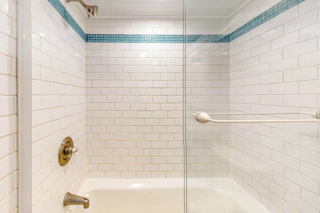A bathroom with white subway tiles, a glass shower enclosure, and a white bathtub.