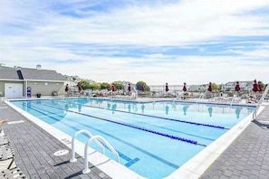Ein Schwimmbecken mit mehreren Bahnen, einem Rettungsschwimmerstand und Liegestühlen.