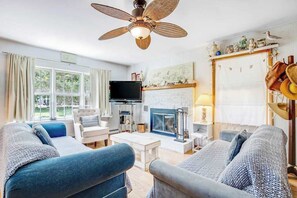 A living room with a sofa, armchairs, a television, a fireplace, and a ceiling fan. - Dog-friendly beach cottage with WiFi, W/D, updated kitchen & outdoor shower (Ocean City)